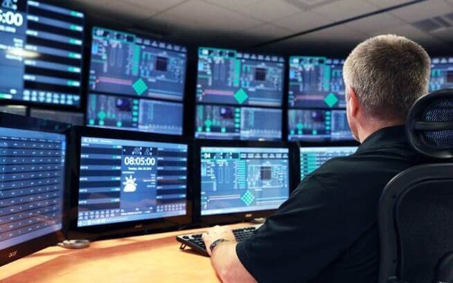 NuScale 2 man wearing a black shirt sitting at a desk typing while looking at a large display of multiple computer monitors